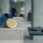 Gold medal on a blue ribbon over a stone podium, with a smartphone and hardware wallet on a counter