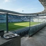 Daylit stadium terraces in blue and slate, with a hardware wallet and coin tray near the foreground rail
