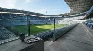 Daylit stadium terraces in blue and slate, with a hardware wallet and coin tray near the foreground rail
