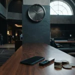 An elegant unmarked twenty-four-hour wall clock above a quiet casino counter, with a phone and coins nearby