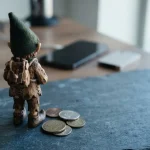 Carved woodland elf figurine seen from behind on a slate counter with a phone and metal coins nearby