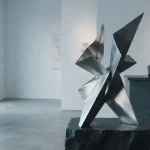 A sculptural metal installation in a daylight gallery with a discreet hardware wallet on a slate side table