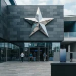 A metal star marquee on a contemporary entertainment building, with a smartphone and payment cards at a nearby counter