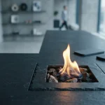 A small vivid flame burns in a dark slate hearth beside a phone and hardware wallet on a modern counter