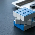Blue, white and grey puzzle cube caught mid-turn, with a hardware wallet and smartphone by a tray