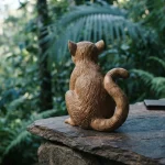 A carved wooden lemur among green jungle leaves, with a hardware wallet and coins on a slate counter in daylight