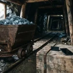 Iron mine cart full of blue-grey crystals in a timber tunnel, with a hardware wallet and smartphone on a crate