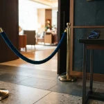 Brass stanchion and blue velvet rope at a lounge entrance, with a smartphone and hardware wallet