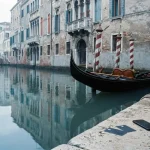 Black gondola moored on a quiet Venetian canal, with payment cards and a smartphone on a stone ledge