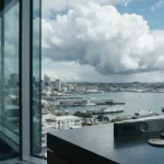 Bright cloud above a blue harbour skyline, with a small hardware wallet on a sunlit counter in the foreground