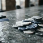 Frosted unbranded casino chips on a cool slate counter with a face-down phone and payment card in the background