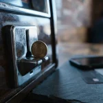Chrome token slot with a brass token about to drop in, with a smartphone and payment cards