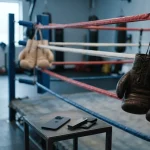 Dark and pale boxing gloves hanging in opposite corners of an empty ring, with a smartphone and hardware wallet ringside