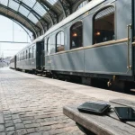 Classic European railway carriage at a sunlit station platform, with a card wallet and smartphone on a bench