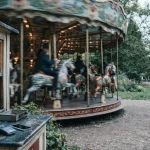 Vintage fairground carousel with carved wooden horses in motion, with a card terminal and smartphone at a ticket booth window