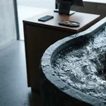 A swirling stream of clear water in a sculpted stone basin, with a phone and loose coins on a counter behind
