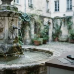 A sculpted stone fountain with water cascading into a basin, with a phone and payment cards on a nearby counter