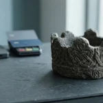 A weathered stone crown on a slate counter with a small hardware wallet and payment cards in the background