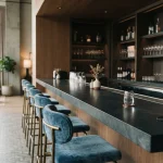 A quiet contemporary lounge bar with blue upholstered stools and an understated card payment counter in daylight