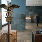 Bronze Roman eagle standard with outstretched wings on a stone plinth, with a smartphone and payment cards by a counter