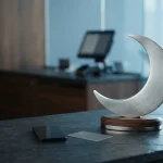 Silver crescent moon sculpture on a slate counter with a smartphone and payment card in a daylight-lit payment studio