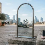 Polished mirror arch in a sunlit stone courtyard, with a hardware wallet and coins on a ledge