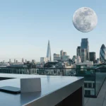 A pale daylight moon above a sleek slate-coloured city rooftop, with a phone and payment card in the foreground
