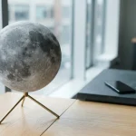 Cratered lunar globe on a brass stand, with a smartphone and payment cards on a cashier counter