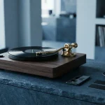 Vintage vinyl record player on a slate counter with a smartphone and payment cards in soft daylight