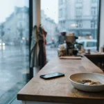 Rain falling beyond a bright cashier counter with a small bowl of coins and a phone resting in the background