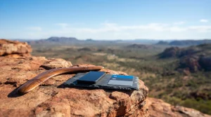 Polished wooden boomerang on a red sandstone ledge, with a smartphone and payment cards on a tray