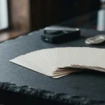 Blank playing cards spread across a slate card table, with a small hardware wallet and loose coins in soft focus