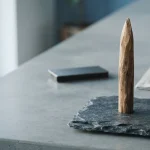 A tapered wooden stake in a slate display block, with a small hardware wallet on a distant counter
