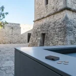 Weathered stone tower beside a modern cashier counter with a small hardware wallet in cool daylight