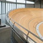 Curving indoor cycling velodrome with a payment counter and unmarked cards softly visible in the distance