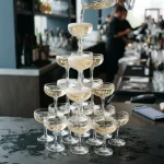 Champagne tower of coupe glasses with golden wine cascading down, with a smartphone and hardware wallet on a cashier counter